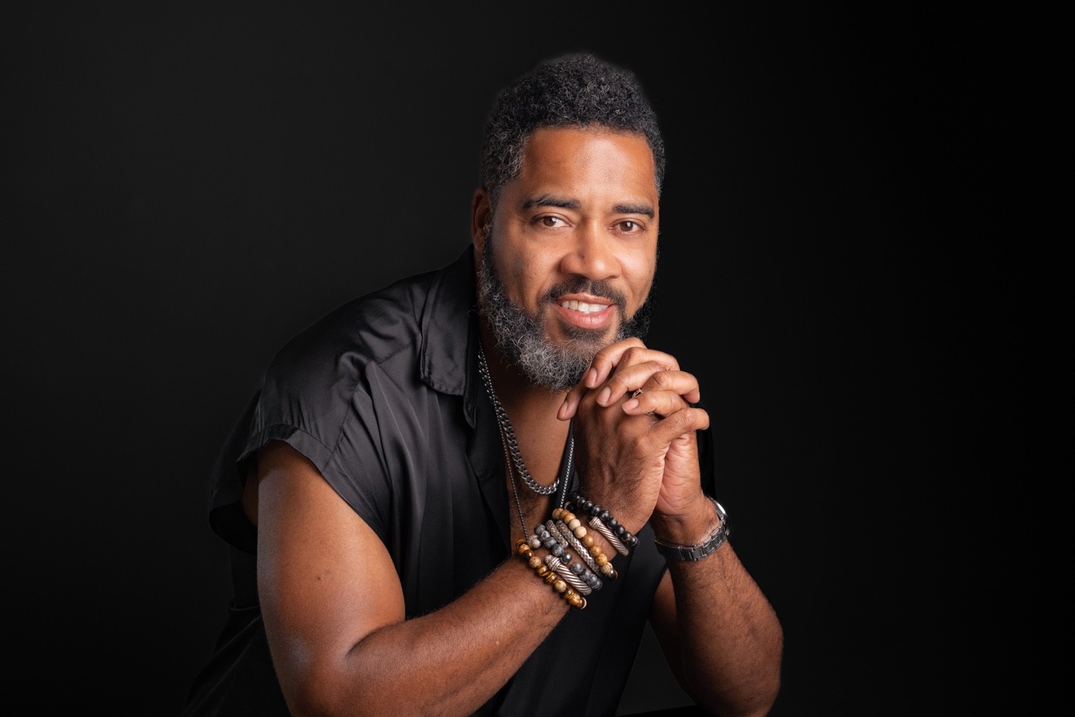Milton Miller smiling in a black shirt with hands clasped