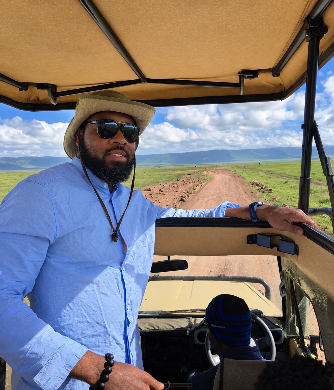 Dr. Milton Miller Jr. in an open safari vehicle overlooking a grassy landscape