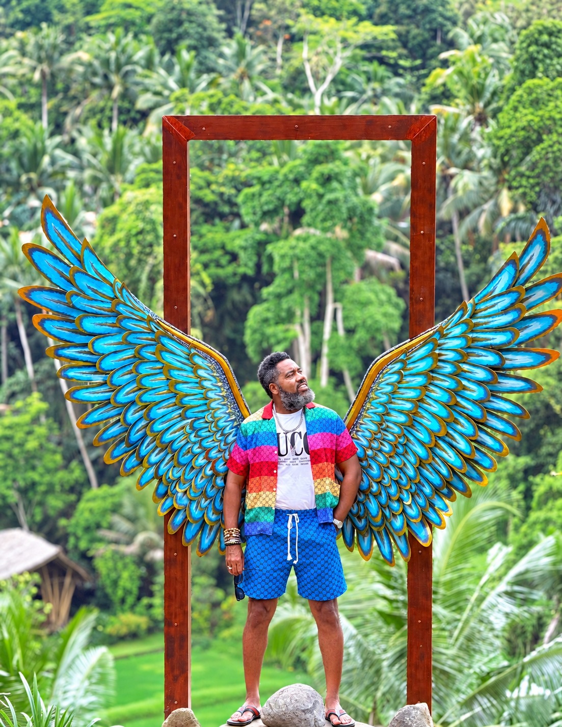 Dr. Milton Miller Jr. beside a blue wing sculpture in a tropical landscape